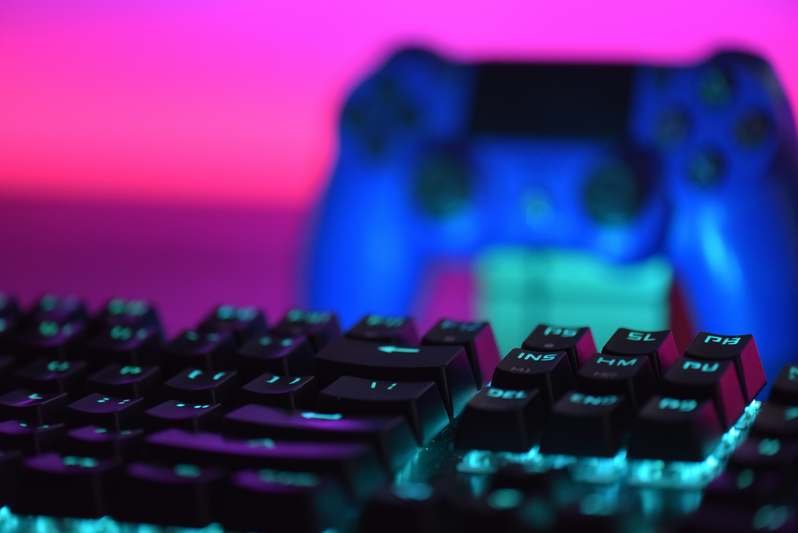 Two gamers discussing a PC controller setup at a desk with keyboards, mice, and multiple controllers